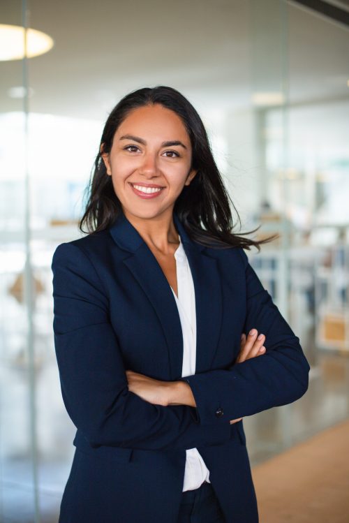 Confident cheerful young businesswoman. Professional business woman standing with crossed arms and smiling at camera inside office building. Business concept